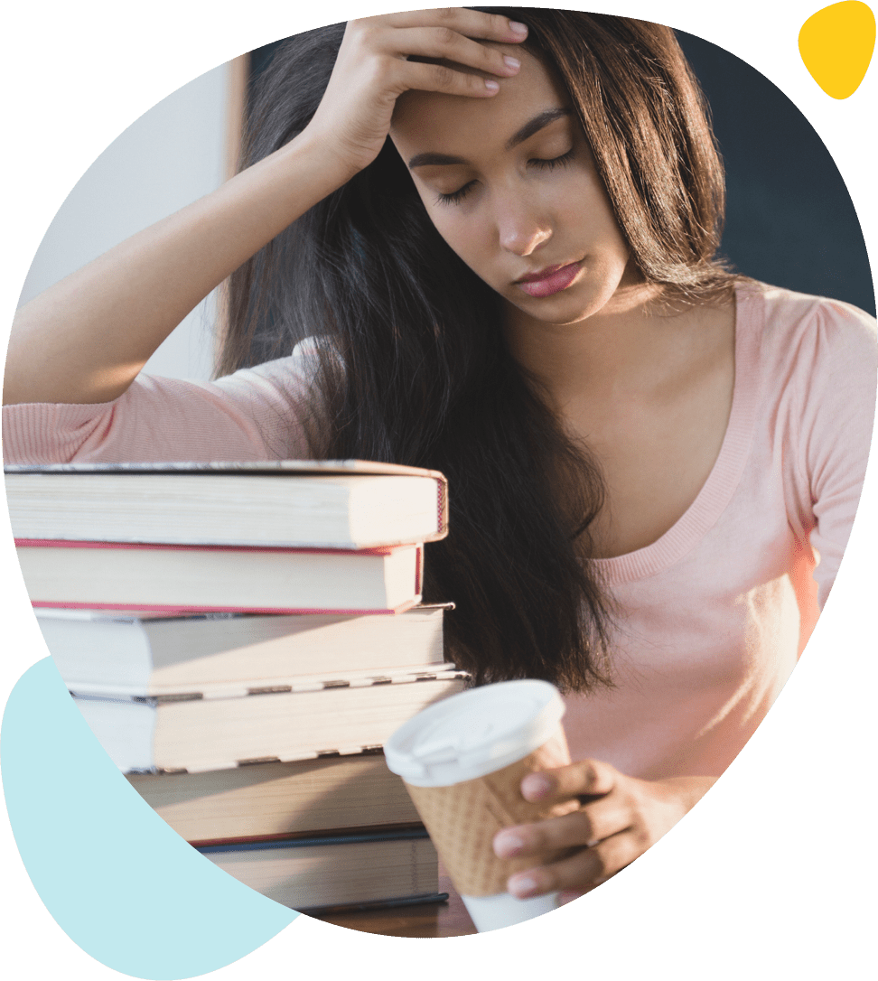Une jeune fille épuisée s'accoude sur ses livres avec un café dans la main